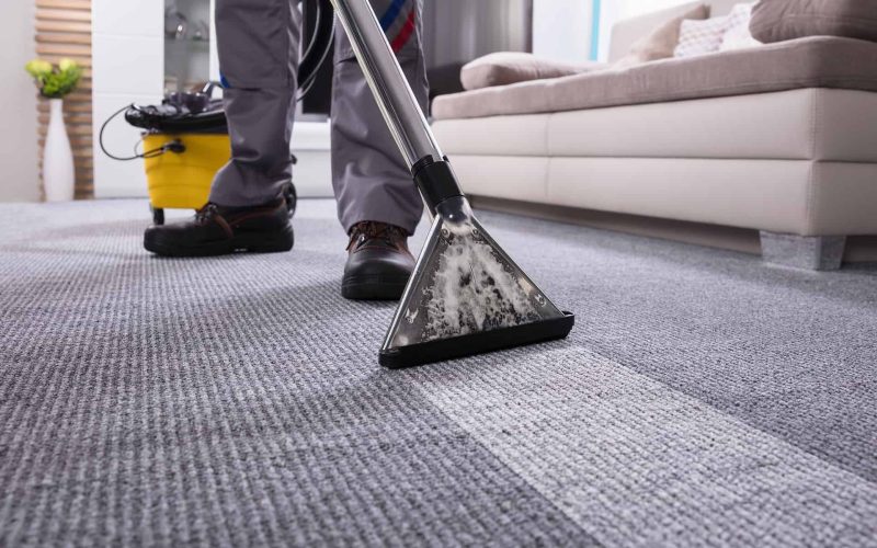 Low Section Of A Person Cleaning The Carpet With Vacuum Cleaner In Living Room