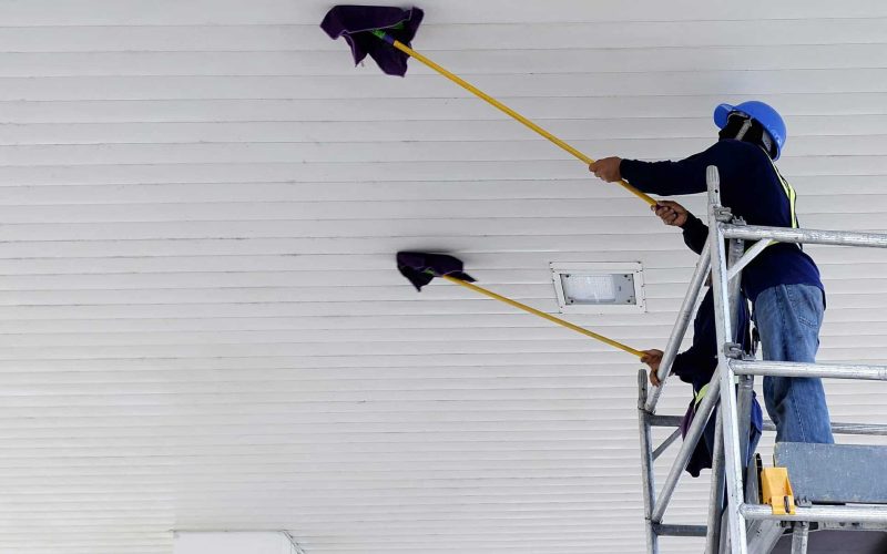 Low angle view of 2 workers on scaffolding using mop sticks to c