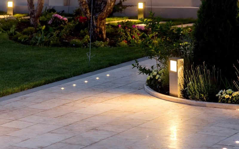 marble tile playground in the backyard of flowerbeds and lawn with ground lantern and lighting in the warm light at dusk in the evening.