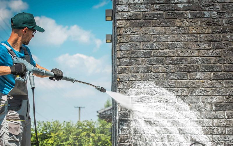 Brick House Wall Pressure Washing with Special Cleaning Detergent. Caucasian Men in His 30s. Taking Care of the Building Elevation.