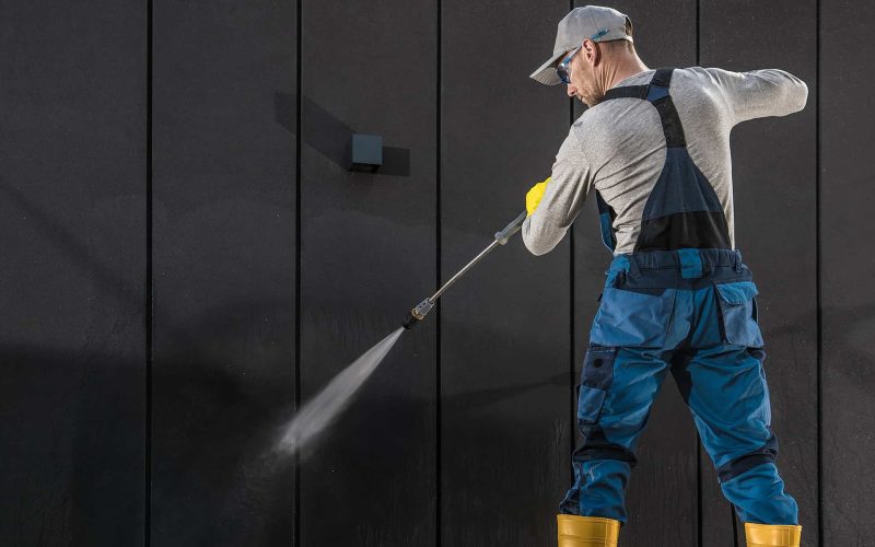 Caucasian Worker in His 40s Cleaning Modern Building Dark Wall Using Powerful Pressure Washer