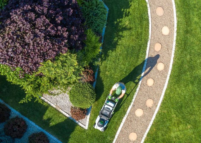 Landscaping Job Grass Mowing Aerial View. Caucasian Gardener with Grass Mower Inside Large Beautiful Backyard Garden.