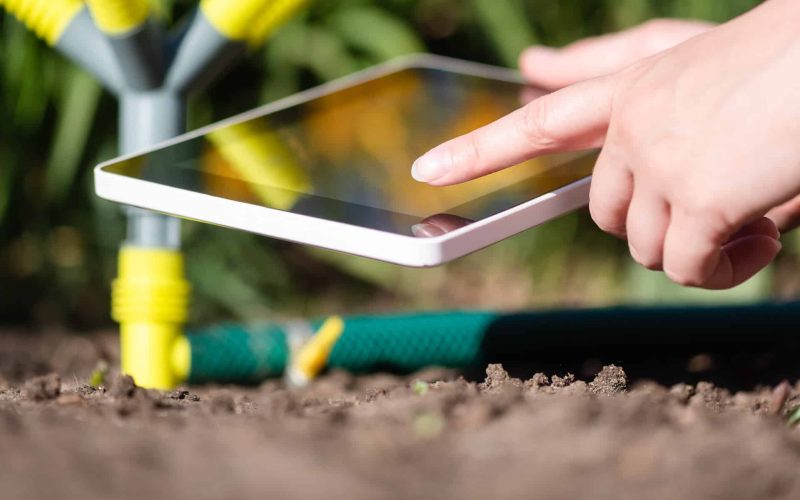 A gardener with a digital tablet using a smart garden application concept. Watering system. Electronic irrigation control.